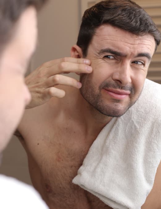A man looking at his skin in a mirror, possibly after a treatment or examining wrinkles